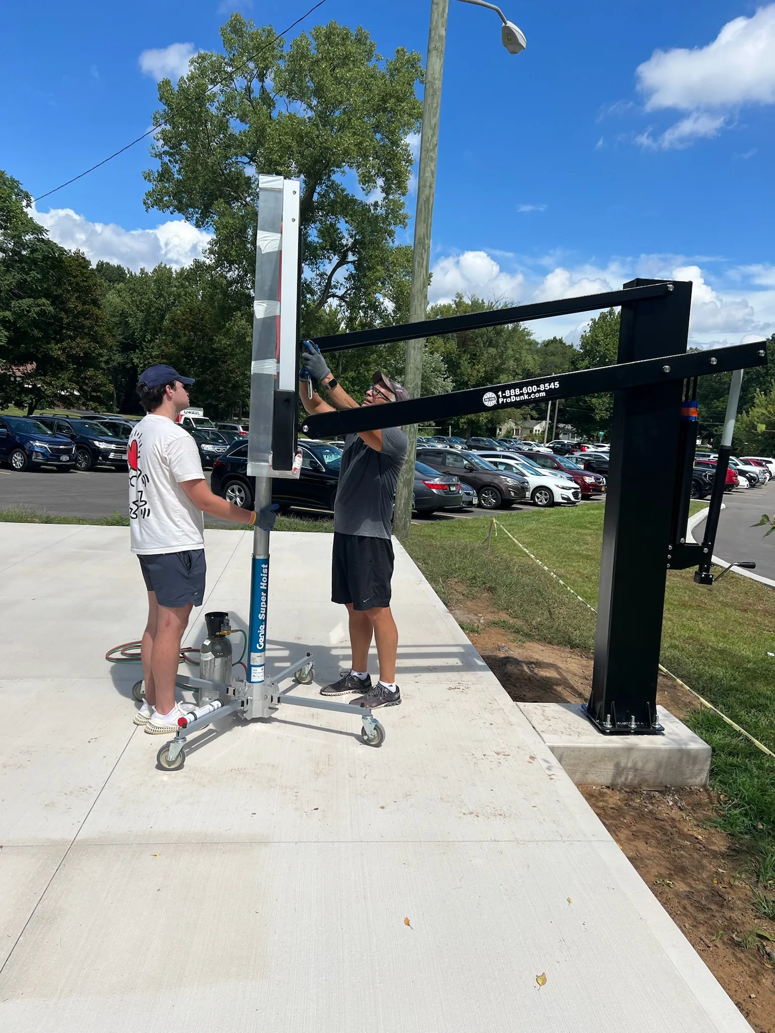 Sport Court WNY installers using a lift to position and secure the support arm for an outdoor basketball hoop during installation.